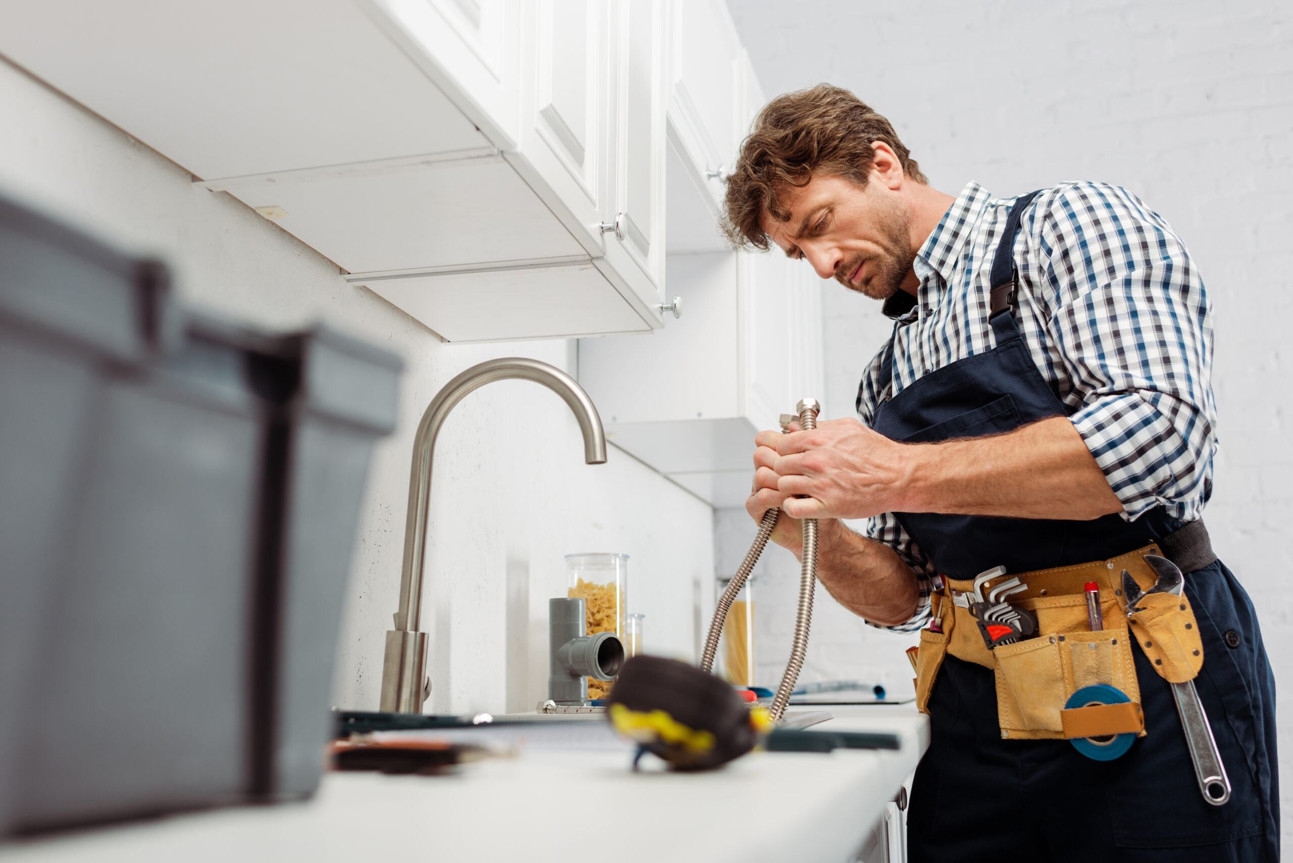 Selective focus of plumber holding metal pipe near kitchen faucet and tools on worktop